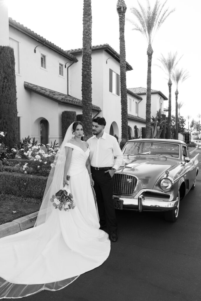Editorial wedding portrait of a bride and groom standing together outside a Tuscan-inspired villa with tall cypress trees.