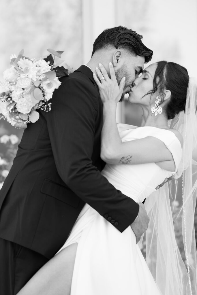Romantic black and white portrait of a bride and groom sharing a kiss on their wedding day.